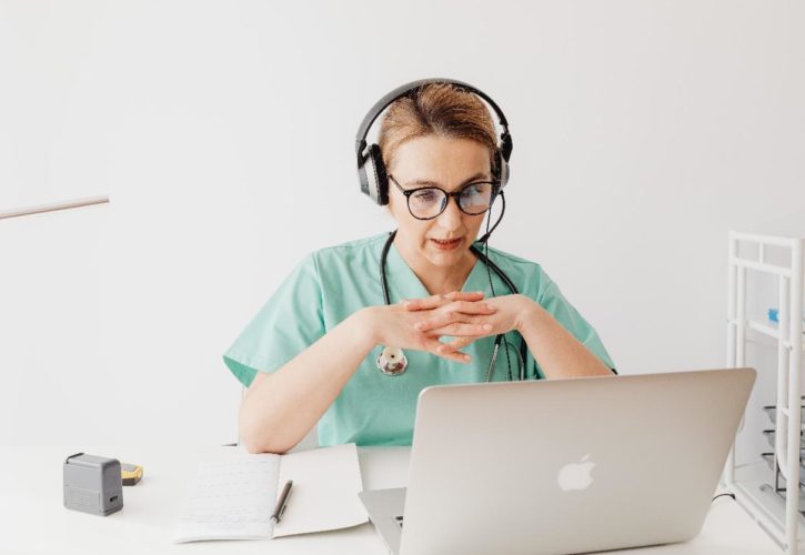 female doctor wearing headset, glasses and stethoscope working with Genie Solutions practice management solution to consult patient on telehealth call.