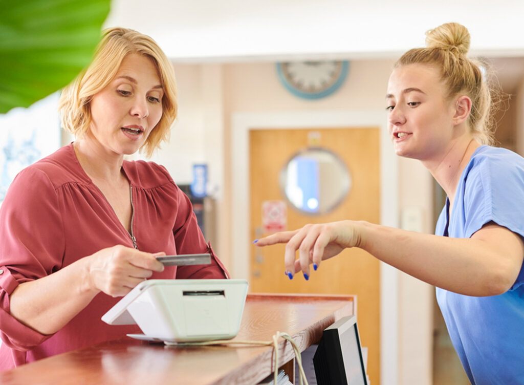 Practice manager and patient using payment terminal at reception area